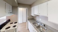 This single-floor residence offers a practical and well-organized layout with a clean, neutral aesthetic throughout. The open living and dining area is finished with light wood-look flooring, a ceiling fan, and large windows fitted with blinds that invite generous natural light. Baseboard heating runs along the perimeter, ensuring comfort year-round. The kitchen is positioned adjacent to the living area and features a white peninsula that provides both workspace and a visual division between the two areas. White cabinetry, granite-look countertops, a double stainless steel sink, an electric range, and a refrigerator equip the kitchen for everyday use. A closet within the kitchen area offers additional storage. The entry hallway connects the living space to the private areas of the home, providing a clear and functional flow. Two bedrooms are each carpeted for comfort, feature ceiling fan fixtures, textured ceilings, and multiple windows with baseboard heating below. The full bathroom includes a tiled tub-and-shower combination with chrome fixtures and a towel ring, maintaining the home's consistent, understated style. Throughout, the warm taupe wall tones and light finishes create a cohesive and inviting atmosphere.