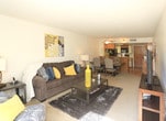 Located on Indian School Road NE in Albuquerque, New Mexico, this single-floor residence offers a functional and comfortable layout across several well-defined living spaces. The living room is generously sized, featuring soft carpeting, neutral-toned walls, and a large window fitted with vertical blinds that allows natural light to fill the space. The open layout connects seamlessly to a dining area, creating an inviting environment for both relaxing and entertaining. The galley-style kitchen is efficiently designed with light wood-finish cabinetry, a full suite of black appliances including a refrigerator, over-range microwave, and electric range, as well as a double sink beneath a skylight panel that brightens the workspace. A wood-toned breakfast bar separates the kitchen from the dining area, adding a casual gathering spot. The bedroom is a restful retreat with plush carpeting and a large sliding glass door with vertical blinds that offers outdoor views and additional natural light. A closet with built-in hanging space provides practical storage. The bathroom features warm hardwood-style flooring, a wide vanity with an extended mirror and built-in lighting, and a full tub-shower combination, creating a clean and comfortable space.