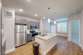 Located at 1720 Summit Crossing Lane in College Station, TX, this 1-bedroom, 1-bathroom unit offers a thoughtfully designed single-floor layout. The open-concept kitchen and living area serves as the heart of the space, showcasing stylish gray shaker cabinets, stainless steel appliances including a refrigerator, electric range, and microwave, and a central island topped with light granite countertops and an integrated sink. Pendant lighting above the island adds a modern touch, while recessed lighting and a ceiling fan keep the living area bright and comfortable. Warm-toned hardwood-style flooring runs throughout the main living areas, complementing the clean, neutral color palette. The bedroom features plush carpeting, warm beige walls, and multiple windows with blinds that allow for natural light while maintaining privacy. A walk-in closet with built-in shelving offers generous storage, and the adjoining bathroom includes granite countertops consistent with the kitchen's design. Additional functionality is provided by a dedicated laundry area and utility room. The overall aesthetic is clean and contemporary, making efficient use of the available space while maintaining a comfortable and inviting atmosphere.