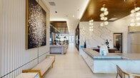 Located at 901 St Albans Dr in Raleigh, NC, this sophisticated amenity space spans a single, expansive floor designed to deliver a premium communal experience. The welcoming entry features a striking marble-clad reception desk accented by an artistic globe pendant chandelier and large-scale wall art, setting an elegant tone from the moment of arrival. The main living lounge area is anchored by soaring ceilings with wood-paneled inlays and brass trim, floor-to-ceiling windows that flood the space with natural light and frame outdoor views, and designer furniture including a geometric black coffee table and sculptural pendant lighting. Adjacent to the lounge, a curated bar and kitchen area showcases a vivid green glazed tile backsplash, dark stone countertops, open wood shelving, and a long island with natural wood barstools beneath a multi-globe chandelier. A dedicated game and entertainment room offers a full-size billiard table, plush green velvet seating, a wall-mounted TV, large-format artwork, and globe pendant lighting throughout. A café-style seating zone features an open, light-filled layout with mixed seating, steel-framed partition screens, and direct access to an outdoor terrace. Together, these thoughtfully designed zones create a dynamic, upscale environment ideal for both socializing and relaxing.