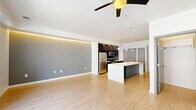 Located at 501 Virginia Ave in Indianapolis, Indiana, this modern single-floor unit offers a thoughtfully designed open-concept layout that seamlessly connects the kitchen and living area. Light hardwood flooring runs throughout, complementing the clean, contemporary aesthetic.

The kitchen is a standout feature, anchored by a large center island with a white quartz countertop, undermount sink, and pendant globe lighting above. Dark espresso cabinetry lines the walls, contrasting elegantly with the white countertops and gray subway tile backsplash. Stainless steel appliances, including a refrigerator, range, and built-in microwave, complete the well-equipped cooking space. A double-door closet adjacent to the kitchen provides ample storage.

The living area is bright and open, featuring a distinctive gray accent wall with integrated LED cove lighting that adds a warm ambient glow. A ceiling fan overhead and sliding glass doors leading to a private balcony allow for natural light and ventilation. Flanking windows with blinds further enhance the airy atmosphere.

The bathroom maintains the same modern sensibility, with wood-toned cabinetry, white quartz countertops, a undermount sink, and light hardwood-style tile flooring. A bathtub and shower combination complete the space. This unit offers a cohesive, contemporary living experience in a compact and efficient footprint.