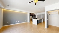 Located at 501 Virginia Ave in Indianapolis, Indiana, this modern single-floor unit offers a thoughtfully designed open-concept layout that seamlessly connects the kitchen and living area. Light hardwood flooring runs throughout, complementing the clean, contemporary aesthetic.

The kitchen is a standout feature, anchored by a large center island with a white quartz countertop, undermount sink, and pendant globe lighting above. Dark espresso cabinetry lines the walls, contrasting elegantly with the white countertops and gray subway tile backsplash. Stainless steel appliances, including a refrigerator, range, and built-in microwave, complete the well-equipped cooking space. A double-door closet adjacent to the kitchen provides ample storage.

The living area is bright and open, featuring a distinctive gray accent wall with integrated LED cove lighting that adds a warm ambient glow. A ceiling fan overhead and sliding glass doors leading to a private balcony allow for natural light and ventilation. Flanking windows with blinds further enhance the airy atmosphere.

The bathroom maintains the same modern sensibility, with wood-toned cabinetry, white quartz countertops, a undermount sink, and light hardwood-style tile flooring. A bathtub and shower combination complete the space. This unit offers a cohesive, contemporary living experience in a compact and efficient footprint.