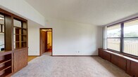 This well-organized 1-bedroom, 1-bathroom unit spans a single floor and features a thoughtfully designed layout that maximizes everyday comfort and functionality. The living area welcomes residents with soft wall-to-wall carpeting, clean white walls, textured ceilings, and warm wood-toned trim and baseboards throughout. A large window floods the space with natural light while offering views of the surrounding exterior, and a dedicated entry door provides a clear sense of arrival.

The kitchen is open to the living space via a wood-trimmed pass-through divider with built-in cabinetry, creating a connected yet defined cooking area. It is equipped with white appliances including a refrigerator, electric range with oven, and a single-basin sink, all complemented by abundant upper and lower cabinetry with white fronts and dark wood framing, as well as durable hardwood-style flooring.

The bedroom is a comfortable, carpeted retreat featuring a ceiling fan with light fixture and a window that brings in natural light. The full bathroom includes a single-sink vanity with a marble-patterned countertop, a tub/shower combination, and hardwood-style flooring. A dedicated laundry area houses a full-size washer and dryer alongside a water heater and electrical panel, adding exceptional convenience to everyday living.