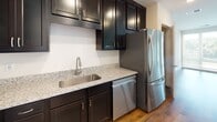 Located at 608 Buttercup Dr in Monroeville, PA, this single-floor unit offers a well-designed layout with a clean, contemporary aesthetic throughout. The open living area is finished with rich hardwood-style flooring and neutral walls, creating a bright and versatile space. Large windows and a glass-panel door provide direct access to a private balcony, flooding the area with natural light and offering pleasant views of surrounding greenery.

The kitchen is a standout feature, outfitted with dark espresso cabinetry that extends floor to ceiling for ample storage. Light granite countertops provide a striking contrast, while stainless steel appliances — including a refrigerator, range, built-in microwave, and dishwasher — complete the functional and polished space. Hardwood-style flooring continues throughout this area.

The bedroom is carpeted for comfort and features a window with outdoor views, recessed HVAC venting, and clean white walls that lend a calm, neutral atmosphere.

The bathroom is finished with a classic black-and-white mosaic tile floor, a dark vanity with a white countertop and large mirror, and a walk-in shower, combining timeless design with practical functionality throughout.