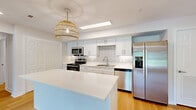 Located at 264 Britishwood Drive in Nashville, TN, this well-appointed 2-bedroom, 2-bathroom single-floor home offers a clean, modern aesthetic throughout. The open-concept living, dining, and kitchen area serves as the heart of the home, bathed in natural light from large windows and a glass patio door. The living room features light hardwood flooring and a ceiling fan, creating a bright and airy atmosphere with pleasant outdoor views. The fully renovated kitchen is a standout, boasting white shaker cabinetry, white quartz countertops, a white subway tile backsplash, stainless steel appliances including a range, microwave, dishwasher, and refrigerator, and a central island with additional prep space, finished with a stylish woven pendant light. Two hallways connect the bedrooms and bathrooms, lined with white panel doors and continued light hardwood flooring. The primary bedroom is generously sized with plush carpeting and a ceiling fan, while the second bedroom offers similar comfort. Both bathrooms are finished in crisp white, one featuring a vanity with white cabinetry and a tub/shower combo. Three closets, an in-unit laundry room, and an outdoor patio round out this well-organized, move-in-ready home.