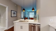 Located on Stockyard Street in Nashville, Tennessee, this single-floor residence offers a thoughtfully designed layout with modern finishes and a cohesive aesthetic throughout. The kitchen is a functional centerpiece, featuring white shaker cabinetry, stainless steel appliances including a full-size refrigerator, range, and microwave, complemented by a decorative patterned tile backsplash and white quartz countertops. A kitchen island with an undermount sink and pendant lighting above connects the cooking space to the open living area, where rich hardwood flooring flows seamlessly underfoot.

The living room benefits from generous natural light admitted through large windows with blinds, and features a calming blue accent wall that adds depth to the neutral palette. The bedroom continues this color scheme, with soft carpeting, ample natural light, and direct access to a well-finished bathroom. The bathroom showcases white cabinetry with matte black hardware, a white quartz vanity, a large mirror, and classic black-and-white mosaic tile flooring. Additional spaces include a secondary room with carpet and a large window. Throughout the unit, the interplay of warm wood tones, cool blue accents, and contemporary fixtures creates a polished, inviting atmosphere.