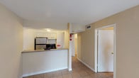 This single-floor unit offers a practical and functional layout designed for comfortable everyday living. The open-concept kitchen anchors the space, featuring a peninsula-style breakfast bar with laminate countertops, white cabinetry, a double-basin sink, a stainless steel refrigerator, and a black electric range — all finished with tile flooring that carries seamlessly throughout the unit.

Adjacent to the kitchen, the main living area is bright and open, bathed in natural light from a large sliding glass door dressed with vertical blinds. The room offers generous wall space and a clean, neutral palette of warm beige tones complemented by crisp white baseboards and a textured ceiling with flush-mount lighting.

A hallway connects the living and kitchen areas to the private quarters of the unit. The bathroom is well-appointed with a wide vanity featuring a single sink, laminate countertop, white cabinetry, and a large mirror with overhead lighting. The toilet and additional fixtures are accessible within the same space. A dedicated closet area provides additional storage.

Tile flooring is consistent throughout all areas of the unit, making maintenance straightforward. The overall design is clean and understated, with a warm neutral color scheme creating a welcoming and move-in ready environment.