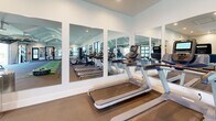 Located at Quarters Landing in Sneads Ferry, NC, this single-story fitness center is a comprehensively designed facility built to support a wide range of training styles and fitness goals. The interior is organized into several distinct workout zones, each tailored to specific exercise disciplines. A standout feature is the large-format glass garage door that opens directly to an outdoor turf training area, seamlessly blending indoor and outdoor fitness spaces and flooding the interior with natural light and fresh air.

The main training floor is anchored by a turf track with yard-line markings, ideal for functional training, sled pushes, and conditioning drills. This area is flanked by a full rack of dumbbells, cable machines, and a multi-functional strength station. Treadmills and elliptical machines line a mirrored wall, maximizing the sense of space while allowing users to monitor their form. A dedicated studio room offers open floor space for cycling, group fitness, or stretching, and is equipped with spin bikes, wall mirrors, and ceiling fans for ventilation.

An additional room provides space for functional accessories including medicine balls, kettlebells, plyo boxes, and step platforms, with a wall-mounted display screen for guided workouts. The outdoor turf area includes battle ropes and a squat rack for open-air training. Clean white walls, recessed lighting, and vaulted ceilings with coffered detailing give the entire facility a bright, modern, and professional atmosphere.