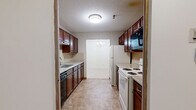 This single-floor residence in Manchester, NH offers a practical and comfortable layout across three bedrooms and two full bathrooms. The galley-style kitchen is outfitted with rich dark wood cabinetry, granite-look countertops, and white appliances including a refrigerator and electric range, complemented by a dishwasher and an elegant chandelier visible through the pass-through. The open living and dining area is generously sized, featuring soft wall-to-wall carpeting, baseboard heating, and a sliding glass door that fills the space with natural light and provides access to an outdoor balcony with lush green views. The spacious primary bedroom also benefits from natural light through a large window overlooking greenery, with baseboard heating and wall-to-wall carpet throughout. The additional bedrooms are well-proportioned, each with plush carpeting and windows. Both bathrooms are finished with warm-toned tile flooring, rich wood vanities with white countertops, and full tub-shower combinations equipped with accessibility grab bars. Multiple hallways connect the rooms efficiently, contributing to a cohesive and easy-to-navigate floor plan throughout this inviting residence.