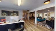 Located at 1920 NE Terre View Drive in Pullman, Washington, this single-story clubhouse facility serves as the community hub for Ruckus Student Living. The space is thoughtfully designed to support both residential services and recreational needs.

The leasing office greets visitors with a clean, modern aesthetic, featuring wood-plank flooring, large windows that allow ample natural light, and a welcoming front desk area flanked by comfortable seating. Display shelving highlights community merchandise and amenities information.

Adjacent to the office, the open common area flows seamlessly into a lounge space appointed with a bold mountain-landscape accent wall, a wall-mounted TV, leather seating, and a geometric-patterned area rug — creating a relaxed yet stylish atmosphere for residents to gather.

The game room is a standout feature, boasting a rustic billiards table, shuffleboard table, and additional lounge seating, all beneath a striking sculptural ceiling installation. Large glass doors connect the space to outdoor areas, enhancing the open feel.

The fitness center is well-equipped with treadmills, a rowing machine, spin bikes, free weights, a weight bench, cable machines, and stability equipment. Floor-to-ceiling windows overlook the outdoor pool and surrounding grounds, providing an energizing workout environment with abundant natural light.