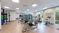 Located at 150 Glover Avenue in Norwalk, Connecticut, this professionally appointed fitness center spans a generous single-floor layout designed to support a wide range of workout activities. The space is bathed in natural light, courtesy of large floor-to-ceiling windows that line the perimeter and offer lush, verdant outdoor views, creating an energizing and open atmosphere throughout.

The main workout floor features durable light wood-tone flooring and is well-equipped with a comprehensive selection of Matrix-brand strength machines, cable systems, and multi-functional training stations. A full row of cardio equipment—including treadmills, ellipticals, and stationary bikes—is positioned along the windowed walls to maximize the connection to the outdoors. Free weight areas include adjustable benches, a dumbbell rack, and plate-loaded stations, catering to varied fitness routines.

Full-length mirrors span entire walls in the strength training zone, enhancing spatial perception and allowing users to monitor their form. A dedicated group exercise and functional training studio features a vibrant blue rubberized floor, turf accents, a large wall-mounted display screen, and ample open space for classes, stretching, or dynamic movement. Recessed panel lighting throughout ensures consistent, bright illumination across all areas. The overall design is clean, modern, and purpose-built for a premium fitness experience.