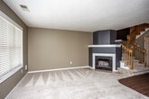 This two-floor residence offers a thoughtfully laid-out interior with a blend of practical and comfortable design elements throughout. The living area serves as a welcoming focal point, anchored by a corner fireplace framed in white trim and gray surround, with plush carpeting underfoot and a textured ceiling overhead. The kitchen is well-equipped, featuring white shaker-style cabinetry extending to the ceiling, granite-look countertops, hardwood-style flooring, and black appliances including a range, microwave, dishwasher, and refrigerator. A window above the sink allows natural light to filter into the space. The bedrooms are generously proportioned, each finished with soft carpeting, neutral warm-toned walls, ceiling fans with light fixtures, and windows fitted with horizontal blinds for privacy and light control. The bathrooms are cleanly finished, with granite-topped white vanities, tile flooring, and large mirrors. One bathroom includes accessibility features such as chrome grab bars, while another offers a full tub and shower combination. A staircase connects the two levels, contributing to the home's multi-story layout. Throughout the space, a consistent warm neutral color palette and clean white trim create a cohesive and inviting atmosphere.