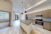 Located at 1050 Blanch St in West Palm Beach, FL, this thoughtfully designed one-bedroom, one-bathroom unit offers a modern living experience within a compact, efficient floor plan. The open-concept kitchen and dining area serves as the heart of the home, showcasing light wood cabinetry, subway tile backsplash, dark quartz countertops, and a full suite of stainless steel appliances including a range, microwave, dishwasher, and French door refrigerator. A central island with pendant lighting adds both function and style, while soaring ceilings amplify the sense of space throughout. Light-toned luxury flooring runs through the main living areas, enhancing the bright and airy ambiance. The living room opens via glass doors to a private patio enclosed by modern metal railings, offering views of lush tropical landscaping. The bedroom features soft carpeting, a large window with natural light, and access to generous closet space with built-in wire shelving systems. The bathroom is finished with large-format marble-style tile in the tub/shower surround, a wood-toned vanity with quartz countertop, and an illuminated frameless mirror. An in-unit laundry area adds everyday convenience to this well-appointed West Palm Beach residence.