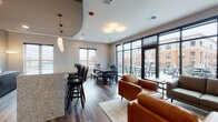 Located at 533 Pinney St in Madison, Wisconsin, this single-floor community space is thoughtfully designed to accommodate a variety of social and functional needs. The open-concept layout seamlessly connects multiple gathering zones, creating an inviting and cohesive environment throughout.

The lounge area serves as a central focal point, furnished with tan leather armchairs and a gray sofa arranged around a wall-mounted flat-screen television. Sconce lighting and recessed fixtures provide warm, even illumination, while wood-look plank flooring runs consistently throughout the space, reinforcing its contemporary aesthetic.

A dedicated dining area features a rustic wood farmhouse-style table paired with dark wood chairs, positioned beneath recessed lighting and flanked by windows that bring in natural light and exterior views. Adjacent to this, a bar-height counter with granite stone surfaces and dark cabinetry offers additional seating with bar stools.

The kitchenette is equipped with granite countertops, dark lower cabinetry, a stainless steel sink, and a wall-mounted television, making it a practical and well-appointed prep area for gatherings.

Floor-to-ceiling black-framed windows and glass doors open directly onto an outdoor terrace furnished with additional seating, extending the usable space and filling the interior with abundant natural light.