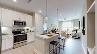 This single-floor residence at 1701 J N Pease Pl in Charlotte, NC, presents a thoughtfully designed open-concept layout with contemporary finishes throughout. The kitchen serves as a central hub, featuring crisp white shaker cabinetry, quartz countertops, a subway tile backsplash, and a full suite of stainless steel appliances including a French door refrigerator, range, microwave, and dishwasher. A spacious island with an undermount sink and bar seating connects the kitchen seamlessly to the living area, where large windows allow abundant natural light to fill the space. The living room offers a comfortable, airy atmosphere accented by a ceiling fan overhead.

The bedrooms are generously sized, each benefiting from large windows with horizontal blinds and ceiling fans. The primary bedroom connects to an en-suite bathroom featuring a dual-sink vanity with white cabinetry and quartz countertops. A secondary bathroom mirrors the same clean aesthetic with a white vanity and light wood-look flooring consistent throughout the residence.

Light wood-look flooring runs continuously across the entire floor plan, unifying the space with a warm, modern tone. The overall ambiance is bright, clean, and contemporary, reflecting a well-appointed and cohesive design sensibility.