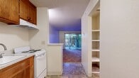 Located at Cambridge Court in Salinas, CA, this 340-square-foot single-floor unit offers an efficient and functional layout comprising a living room, hallway, and full bathroom. The living area is generously carpeted and features a textured ceiling, neutral white walls, and a sliding glass door fitted with vertical blinds that fills the space with natural light and provides access to an outdoor area with greenery views. A built-in pass-through breakfast bar separates the living space from the kitchen nook, which includes warm wood-tone upper cabinetry, a white refrigerator, and tile flooring. A floor-mounted heating/ventilation unit is also present in the living area. The hallway connects the main living space to the bathroom, which is finished with earth-toned tile flooring, a white single-sink vanity with under-cabinet storage, a toilet, and a full-size soaking bathtub. Bright, clean white walls throughout the bathroom enhance its open feel. The unit's straightforward design prioritizes practicality, making it a well-organized and self-contained living space suitable for a single occupant.