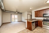This single-floor residential unit offers a well-designed, open-concept layout that blends functionality with comfort. The kitchen is a standout feature, outfitted with rich dark wood cabinetry, granite-style countertops, stainless steel appliances including a side-by-side refrigerator, an electric range, and a dishwasher. A peninsula counter provides a natural transition into the adjoining living area, which is finished with plush carpeting and a ceiling fan overhead. Sliding glass doors open directly onto a private balcony, filling the space with natural light and offering views of the surrounding outdoor scenery.

A distinctive architectural detail throughout the unit is the exposed cylindrical ductwork running along the upper walls, lending an industrial character to the otherwise residential aesthetic. Rich dark wood baseboards and door trim provide consistent, warm contrast against the neutral-toned walls.

The bedrooms are generously sized, each carpeted and featuring built-in closets with shelving and rod systems for organized storage. Windows with vertical blinds allow natural light to filter in while maintaining privacy. The bathroom is clean and functional, featuring a full soaking tub with a tiled surround. The unit's thoughtful layout and blend of practical finishes make it a comfortable and versatile living space.