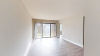 This single-floor residence offers a clean, modern aesthetic throughout, characterized by neutral warm-toned walls, crisp white baseboards, and light wood-look flooring that flows consistently across the living spaces. The spacious main living area is a standout feature, bathed in natural light from large sliding glass doors that frame views of mature trees and greenery, creating a seamless indoor-outdoor connection. Vertical sheer curtains provide a soft, elegant touch to the expansive glazed wall, while an additional side window further brightens the space.

A bedroom features vaulted ceiling details with an exposed beam accent and a ceiling fan with integrated lighting, adding both character and comfort. The neutral palette and open layout lend the room a versatile and airy quality.

The kitchen is outfitted with rich dark cabinetry, granite-style countertops, and a stainless steel sink, providing a practical and attractive workspace. Conveniently tucked beside the kitchen is a dedicated laundry nook housing a stacked washer and dryer unit, maximizing space efficiency.

The bathrooms are finished with matching dark wood vanities, stone-tone countertops, and mirrored medicine cabinets. Light wood-look flooring continues into these spaces, maintaining a cohesive design language. The overall ambiance of the residence is clean, bright, and move-in ready.