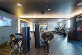 Located at 3310 S Tryon St in Charlotte, North Carolina, this modern fitness center offers a generously sized, single-floor space designed to support a full range of workout routines. The facility features a thoughtfully zoned layout that separates cardio and strength training areas, allowing for efficient use of the space throughout.

The cardio zone is outfitted with multiple treadmills, elliptical trainers, stair climbers, and stationary bikes, all positioned alongside large windows that invite natural light and provide views of the surrounding area. The strength training section includes professional-grade Hoist cable machines and selectorized equipment, a dedicated free weights area with a full dumbbell rack and adjustable benches, and a functional training zone stocked with medicine balls, kettlebells, and stability balls.

The interior design balances a contemporary aesthetic with a performance-focused environment. Cove lighting runs along the ceiling perimeters, casting a warm ambient glow over the dark-toned flooring. Large mirrors along the walls visually expand the space and assist with form during workouts. Recessed lighting complements the natural light from the floor-to-ceiling windows. The overall ambiance is modern and professional, well-suited to support a wide variety of fitness goals.