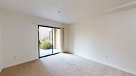 Located at 10150 Torre Ave in Cupertino, California, this single-floor unit offers a well-organized layout with clean, neutral finishes throughout. The living area is generously proportioned, featuring plush wall-to-wall carpeting, crisp white walls, and a large sliding glass door that fills the room with natural light while providing direct access to a private patio. Views of lush greenery and mature trees create a tranquil outdoor connection. A baseboard heating unit and wall-mounted thermostat ensure year-round comfort.

The kitchenette is efficiently designed with warm wood cabinetry, stone-look countertops, an under-cabinet range hood, a sink, and a full-size white refrigerator. The open transition between the kitchen and living areas supports a functional, cohesive flow throughout the unit.

The bedroom is carpeted and quietly positioned, featuring a pull-cord call system, indicating this unit may be part of a senior or assisted living community. The bathroom has been tastefully updated with large-format tile flooring in warm earth tones, a white vanity with a framed mirror, stylish vanity lighting, and a glass-enclosed shower stall. The overall ambiance of the space is calm, clean, and practical, making it a comfortable and low-maintenance residence in the heart of Cupertino.