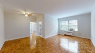 Located at 4540 MacArthur Blvd NW in Washington, DC's desirable Georgetown/Palisades neighborhood, this two-bedroom, one-bathroom unit offers a well-organized single-floor layout. Warm parquet wood flooring flows throughout the living areas and bedrooms, lending a classic character to the space. The living room is generously proportioned, featuring crown molding, a ceiling fan with light fixture, and clean white walls that create a bright, neutral backdrop. Natural light filters in through multiple windows equipped with blinds, giving each room an airy feel. The kitchen is efficiently designed with white cabinetry, granite-look countertops, a stainless steel sink, a gas range, and light tile flooring. A window above the counter brings in natural light and ventilation. Both bedrooms continue the parquet flooring theme and offer good natural light through well-placed windows, with radiator heating units present. The primary bedroom is comfortably sized with room for a full furniture arrangement. The bathroom is clean and functional, featuring a full tub and shower combination with white tile surround and a window for natural ventilation. A connecting hallway ties the rooms together, providing a practical and cohesive flow throughout this efficiently laid-out Washington, DC residence.