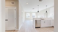 This thoughtfully designed 2-bedroom, 2-bathroom residence offers a clean, modern aesthetic throughout its single-floor layout. Light-toned hardwood flooring flows seamlessly across the open-concept living and kitchen areas, creating a bright and cohesive atmosphere. The kitchen is a standout feature, equipped with sleek white flat-panel cabinetry, a white quartz countertop island with an integrated sink, stainless steel appliances including a refrigerator, range, microwave, and dishwasher, and a white subway tile backsplash. A stylish black pendant light adds a contemporary accent overhead. The living area extends from the kitchen, bathed in natural light from multiple windows offering outdoor neighborhood views. Both bedrooms are generously proportioned, featuring the same light hardwood flooring, neutral warm-toned walls, and large windows that invite ample sunlight and scenic views. The spacious primary bedroom includes two windows framing elevated outdoor vistas. The two bathrooms are finished with marble-patterned tile flooring and wall surrounds, white floating vanities with quartz countertops, gold-toned hardware, and frameless mirrors. A dedicated closet provides additional storage, completing this well-appointed residence.