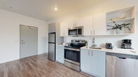 Located in the NW District of Portland, Oregon, this 2-bedroom, 1-bathroom unit offers a clean, modern design across a single floor. The open living and dining area features wood-style plank flooring and large windows that bring in generous natural light and views of the surrounding neighborhood. A ceiling fan adds practical comfort to the main living space.

The kitchen is well-appointed with stainless steel appliances, including a range, over-the-range microwave, refrigerator, and dishwasher. White cabinetry with modern hardware provides ample storage, and the layout flows efficiently into the main living area.

The primary bedroom includes a dedicated window with neighborhood views and continues the wood-style flooring found throughout the unit. The second bedroom is bright and minimalist, featuring clean white walls and additional windows. A wall-mounted mini-split HVAC unit provides climate control in the living area.

The bathroom is finished with wood-style flooring, a full tub-shower combination, and white cabinetry. The overall aesthetic throughout the unit is contemporary and neutral, with white walls and consistent flooring creating a cohesive, light-filled environment suited for urban living in Portland.