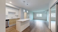 This well-appointed two-bedroom residence in West Kelowna offers a thoughtfully designed single-floor layout with modern finishes throughout. The open-concept living and kitchen area serves as the heart of the home, featuring warm wood-look vinyl plank flooring that extends seamlessly across the space. The kitchen is outfitted with two-tone cabinetry — combining crisp white upper cabinets with natural wood-grain lower cabinets — complemented by a classic white tile backsplash, a sleek white quartz countertop, a double stainless steel sink, and a central island with pendant lighting above. Stainless steel appliances complete the kitchen's contemporary look. The living area benefits from a large window that draws in natural light and offers views of the surrounding neighbourhood. Both bedrooms are carpeted for comfort; the generously sized primary bedroom features mirrored sliding closet doors, while the second bedroom also includes a window with outdoor views. A dedicated laundry room houses a heat pump water heater, and the space benefits from recessed lighting throughout. Clean white walls and modern trim tie the entire home together into a cohesive, move-in-ready package.