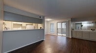 This single-floor residential unit offers a well-organized layout that balances open communal spaces with comfortable private quarters. The living area is a standout feature, showcasing rich, dark hardwood flooring that extends throughout the main living and dining zones. Neutral gray walls and a textured ceiling complement the space, while a sliding glass door and an adjacent window flood the room with natural light and provide direct access to an outdoor balcony.

The kitchen is designed in a galley style, featuring light gray cabinetry, marble-look countertops, a double sink, a dishwasher, and a full-size refrigerator. A pass-through counter connects the kitchen to the living area, creating an open, communicative flow between the two spaces.

The bedrooms are carpeted for comfort and each include ceiling fans with light fixtures and window treatments for privacy. One bedroom offers its own sliding glass door leading to the balcony, adding an additional connection to the outdoors.

The bathroom is finished with large-format stone-look tile surrounding a full soaking tub and shower combination, giving it a clean and polished appearance. The entryway features the same dark hardwood flooring found throughout the main living areas, providing a cohesive welcome into the unit.