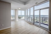 Located on a high floor at 20 George Street in downtown Hamilton, this contemporary 2-bedroom, 2-bathroom unit offers an impressive blend of modern design and breathtaking panoramic views. Light wood-toned flooring flows throughout, complementing the clean white walls and creating a bright, cohesive aesthetic.

The open-concept living area is defined by expansive floor-to-ceiling windows that flood the space with natural light and frame stunning views of the Hamilton cityscape and Lake Ontario. A sliding glass door leads to a balcony, extending the living space outdoors. A distinctive architectural column adds a refined structural accent to the living room.

The kitchen features a central island with a wood-finish base and white countertop, providing both workspace and a natural divider between the kitchen and living areas. Custom wood-panel cabinetry adds warmth to the space.

The primary bedroom is generously proportioned, benefiting from large windows with sweeping city views and a built-in wood-toned closet with matte black hardware. The second bedroom also enjoys elevated views and includes a sliding wood-panel closet. Both bathrooms are finished in a clean, modern style — one with a frameless glass shower and wood-finish vanity, the other with a full soaker tub and white tile surround.