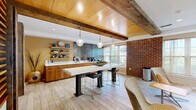 Located at 2432 Albany Ave in West Hartford, CT, this thoughtfully designed single-floor space masterfully combines rustic charm with contemporary finishes. The open layout encompasses a living room and kitchen, unified by light wood-plank flooring that flows seamlessly throughout.

The living room is bright and welcoming, featuring a tray ceiling with recessed lighting, large windows dressed in sheer curtains that invite abundant natural light, and exposed rustic wooden posts that anchor the space with warmth and character. A distinctive slatted wood partition adds architectural interest while defining the transition between areas.

The kitchen is a standout, showcasing warm walnut cabinetry with sleek hardware, a crisp white countertop, and a striking metallic accent wall that serves as a dramatic backdrop. Open floating shelves display curated décor and greenery, adding personality and depth. A central island with pendant lighting and bar seating creates an inviting gathering spot. A prominent exposed wooden beam spans the ceiling above, reinforcing the space's rustic-modern aesthetic. An original brick accent wall adds texture and a nod to the building's heritage.

Together, the rooms create a cohesive, design-forward environment that balances industrial and natural elements with modern comfort — ideal for both relaxed lounging and casual entertaining.
