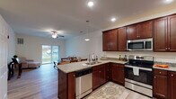 This single-floor residence offers a thoughtfully designed open-concept layout that seamlessly connects the kitchen, dining, and living areas. The kitchen is a standout feature, showcasing rich dark mahogany cabinetry, granite countertops, a central island with a built-in sink, and a full suite of stainless steel appliances including a range, microwave, and dishwasher. Pendant lighting and recessed fixtures illuminate the space, while light hardwood-style flooring ties the common areas together cohesively.

The adjacent dining area comfortably accommodates a full dining set, and the open living room benefits from generous natural light streaming through large sliding glass doors that lead to a private balcony with outdoor views. A ceiling fan adds comfort to both the living area and the bedrooms.

The bedrooms are carpeted and spacious, featuring large windows that invite natural light, ceiling fans, and neutral wall tones that create a calm, versatile atmosphere. The bathroom is well-equipped with a wide vanity topped with a light countertop, rich wood cabinetry, a large mirror, and hardwood-style flooring, providing a clean and functional space. Throughout the residence, neutral tones and consistent finishes contribute to a cohesive, modern aesthetic.