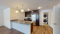 Located at 417 Church Ave in Verona, Wisconsin, this single-floor unit offers a thoughtfully designed layout with contemporary finishes throughout. The open-concept living and kitchen area serves as the heart of the space, where rich hardwood-style flooring flows seamlessly underfoot, complementing the clean, neutral wall tones. Large windows allow natural light to fill the living area, creating a bright and welcoming atmosphere.

The kitchen is well-appointed with dark espresso cabinetry reaching toward the ceiling for ample storage, granite-style countertops, and a full suite of stainless steel appliances including a refrigerator, electric range, and built-in microwave. A peninsula with an undermount sink and pendant globe lighting above adds both function and style, providing additional workspace and casual seating potential.

Conveniently positioned adjacent to the kitchen is an in-unit laundry area with a stacked washer and dryer. The bedroom features plush carpeting, a closet with sliding doors, and a window for natural light. The bathroom includes a tub-shower combination, a dark-cabinetry vanity with stone-look countertop, and tile-style flooring. An attached garage with an automatic opener provides secure, private parking.
