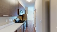 Located at Harbor Point in Stamford, Connecticut, this studio offers a well-designed single-floor layout that maximizes functionality and style. The galley-style kitchen is a standout feature, outfitted with rich dark wood cabinetry, crisp white countertops, and a full suite of stainless steel appliances including a gas range, built-in microwave, dishwasher, and refrigerator with water dispenser. The kitchen flows seamlessly into the open living area, which is finished with warm hardwood-style flooring that extends throughout the unit, lending a cohesive and modern aesthetic. The living space is bright and airy, with large floor-to-ceiling windows that invite abundant natural light and offer expansive city views — a hallmark of this elevated Harbor Point address. The bathroom is thoughtfully appointed with light large-format tile flooring, a tub-shower combination with white subway tile surround, and a dark wood vanity with clean white countertop and gold-toned hardware accents. Neutral wall tones throughout create a versatile backdrop, while the smart layout ensures ample storage and comfortable everyday living in this contemporary Stamford studio.