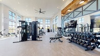 Located at 3144 Old Franklin Road in Antioch, TN, this well-appointed fitness center offers a bright, open, and energizing environment designed for a comprehensive workout experience. The space spans a generous single floor and is defined by soaring double-height ceilings that create an airy, expansive atmosphere throughout.

Large, floor-to-ceiling windows line the walls, flooding the interior with abundant natural light and offering views of the surrounding outdoor areas. The light-toned wood-plank flooring complements the crisp white walls, while warm reclaimed wood accents and industrial-style steel-framed mirror panels add character and visual depth to the space.

The main workout area is thoughtfully divided into distinct zones. The strength training section is equipped with a multi-station cable machine, a full dumbbell rack, adjustable benches, and a cable pulley system. A large flat-screen television is mounted prominently for entertainment during workouts. The cardio zone features multiple treadmills, elliptical machines, a stair climber, and spin bikes, all positioned to take advantage of the expansive window views.

A secondary room provides a more intimate setting, featuring a curved treadmill and spin bike against a vibrant, artfully decorated accent wall. Recessed lighting, an oversized ceiling fan, and direct access to an adjacent outdoor lounge area round out this well-designed, community fitness facility.