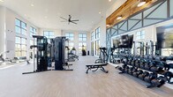 Located at 3144 Old Franklin Road in Antioch, TN, this well-appointed fitness center offers a bright, open, and energizing environment designed for a comprehensive workout experience. The space spans a generous single floor and is defined by soaring double-height ceilings that create an airy, expansive atmosphere throughout.

Large, floor-to-ceiling windows line the walls, flooding the interior with abundant natural light and offering views of the surrounding outdoor areas. The light-toned wood-plank flooring complements the crisp white walls, while warm reclaimed wood accents and industrial-style steel-framed mirror panels add character and visual depth to the space.

The main workout area is thoughtfully divided into distinct zones. The strength training section is equipped with a multi-station cable machine, a full dumbbell rack, adjustable benches, and a cable pulley system. A large flat-screen television is mounted prominently for entertainment during workouts. The cardio zone features multiple treadmills, elliptical machines, a stair climber, and spin bikes, all positioned to take advantage of the expansive window views.

A secondary room provides a more intimate setting, featuring a curved treadmill and spin bike against a vibrant, artfully decorated accent wall. Recessed lighting, an oversized ceiling fan, and direct access to an adjacent outdoor lounge area round out this well-designed, community fitness facility.