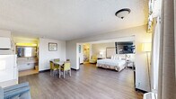 Located at 1400 W Tunnel Blvd in Houma, Louisiana, this well-appointed hotel suite offers a comfortable and functional layout across a single floor. The expansive bedroom is the centerpiece of the suite, featuring wood-style flooring, a textured ceiling, large windows with drape treatments that allow ample natural light, a wall-mounted flat-screen TV, and individual climate control units. A seating area with a sofa complements the sleeping space, adding to the room's versatility.

The suite includes four bathrooms, each finished with warm beige tile work, tub-shower combinations with curtains, and clean, well-lit vanity areas. The vanities feature wide countertops with integrated sinks, framed mirrors, bright overhead lighting, and practical amenities such as hair dryers, towel hooks, and luggage racks — all reflecting a thoughtful hospitality design.

A dedicated dining area just off the main living space features a rectangular table with four upholstered chairs in a chartreuse tone, adding a pop of color against the neutral walls. Subtle decorative wall art enhances the welcoming atmosphere. The overall design is clean and functional, catering to guests seeking a comfortable extended-stay or short-term lodging experience in Houma, Louisiana.