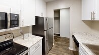 This single-floor apartment at 22306 City Center Dr in Hayward, California offers a well-designed layout with a seamless blend of comfort and modern updates throughout. The open living and dining area is anchored by rich wood-style flooring and a ceiling fan, creating a welcoming atmosphere filled with natural light. A pass-through window connects the main living space to the kitchen, which features white cabinetry, granite-style countertops, stainless steel appliances including a refrigerator and microwave, and a stainless steel sink — all finished with clean, contemporary hardware. A convenient pantry closet with built-in shelving adds practical storage directly off the kitchen. The bedroom is carpeted for warmth and comfort, offering generous proportions and a large sliding glass door that opens to a private balcony overlooking lush, mature trees — a serene and green outlook. A second sliding glass door in the living area also accesses this outdoor space, enhancing the indoor-outdoor connection. The bathroom area features a dual-sink vanity with granite-style countertops, white cabinetry, and a separate water closet for added privacy. Throughout the unit, neutral tones, textured ceilings, and wood-style flooring create a cohesive and move-in-ready aesthetic.
