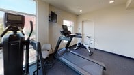 Located at 510 El Cerrito Plaza in El Cerrito, CA, this fitness center is a well-appointed, single-floor facility designed to support a variety of cardio-focused workouts. The space is outfitted with a selection of commercial-grade equipment, including treadmills, an elliptical trainer, and Spinning stationary bikes, all positioned on durable rubber-composite flooring suited for high-traffic exercise use.

A standout feature of the fitness center is its floor-to-ceiling corner windows, which flood the space with natural light and provide open views of the surrounding El Cerrito neighborhood and treetops beyond. The bright, airy atmosphere is complemented by clean, neutral-toned walls that give the room a modern and professional feel.

Additional amenities include a wall-mounted television for entertainment during workouts, wall-mounted hand sanitizer dispensers, and a small waste receptacle for convenience. A yoga mat is also available on-site for stretching or floor exercises. Recessed ceiling lighting ensures the space remains well-lit even when natural light is limited.

The room is compact yet efficiently organized, making practical use of its footprint while maintaining clear circulation paths between equipment. Security is supported by a ceiling-mounted camera. The fitness center is accessed through a dedicated door, offering a self-contained environment for focused exercise.