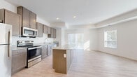 This single-floor unit showcases a clean, contemporary design with a neutral color palette and a thoughtful layout. The open-concept kitchen and living area forms the heart of the space, where light hardwood-style flooring runs continuously underfoot. The kitchen is well-appointed with taupe cabinetry, granite countertops, stainless steel appliances — including a range, microwave, dishwasher, and refrigerator — and a central island that provides additional prep and seating space. Sliding glass doors in the living area invite natural light and offer outdoor access.

The bedrooms are carpeted for comfort and connected via a hallway with coordinating panel doors fitted with brushed gold hardware. One bedroom features a generous walk-in closet outfitted with multi-tier wire shelving systems. The bathroom continues the granite theme with an undermount sink vanity, a large mirror, and brushed nickel fixtures. Multiple windows throughout the unit ensure consistent natural light across all rooms, contributing to a bright and airy atmosphere overall.