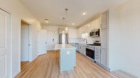 This thoughtfully designed one-bedroom, one-bathroom unit offers a modern aesthetic across its efficiently arranged single floor. The open-concept kitchen serves as the centerpiece of the living area, showcasing two-tone shaker-style cabinetry in white and light gray, a white quartz countertop island with pendant lighting overhead, and a full suite of stainless steel appliances including a gas range, microwave, refrigerator, and dishwasher. A white subway tile backsplash and matte black fixtures complete the kitchen's contemporary look. Light wood-tone luxury vinyl plank flooring runs throughout the main living areas, enhancing the bright, airy feel of the space.

The living area flows naturally from the kitchen toward a large sliding glass door that opens to a balcony, offering elevated outdoor views of the surrounding cityscape. The bedroom features plush carpeting, neutral walls, and a generously sized window that frames expansive outdoor views and fills the room with natural light. A dedicated closet provides practical storage. The bathroom is finished with a gray shaker vanity, white quartz countertop, matte black hardware, a large mirror, and a glass-enclosed walk-in shower with wood-look flooring, creating a clean and cohesive design throughout.