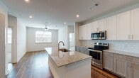 This well-appointed single-floor residence showcases a thoughtfully designed open-concept layout that seamlessly connects the kitchen and living areas. The kitchen serves as the centerpiece of the home, anchored by a large island with a granite countertop and an undermount sink. Cabinetry features a two-tone design — crisp white upper cabinets paired with warm taupe lower cabinets — complemented by a classic subway tile backsplash and a full suite of stainless steel appliances, including a range, microwave, and refrigerator. Rich hardwood-style flooring flows throughout the main living spaces, adding warmth and visual continuity. The living area is illuminated by natural light from a large window and is outfitted with a ceiling fan for year-round comfort. Bedrooms offer plush carpeting underfoot and windows for natural light. The bathroom includes a combination tub and shower, a granite-topped vanity with taupe cabinetry, and hardwood-style flooring. Storage is a standout feature, with multiple spacious walk-in closets offering double hanging rods and built-in shelving. Recessed lighting throughout the unit provides a clean, modern ambiance, rounding out this functional and stylish living space.