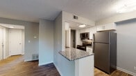 Located at 11605 Nansemond Dr in Louisville, KY, this single-floor residence offers a cohesive, updated interior with a neutral color palette and wood-look flooring throughout most of the space. The kitchen serves as a functional centerpiece, featuring granite countertops, white shaker-style cabinetry, a subway tile backsplash, and a full suite of stainless steel appliances including a refrigerator, electric range, and built-in microwave. A peninsula with a granite overhang extends into the living area, creating a natural transition between cooking and living spaces. The living area is generously proportioned, with French doors flanked by a window that fill the room with natural light and provide views of mature surrounding trees. The bedroom is carpeted and benefits from a window that brings in additional natural light. The bathroom is well-appointed with a granite-topped vanity, wood-look flooring, and a tub-shower combination finished with large-format marble-style tile. Throughout the unit, consistent finishes and a clean, modern aesthetic create a cohesive and comfortable living environment.