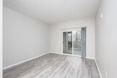 This single-floor unit is designed with a straightforward, functional layout that makes efficient use of its space. The entryway opens to a main living area finished with light wood-style laminate flooring and neutral taupe-toned walls, creating a clean and cohesive aesthetic throughout. Structural columns and well-placed hallways give the space a defined sense of flow between rooms.

The kitchen is equipped with stainless steel appliances, including an electric range and an over-the-range microwave. Light maple-toned cabinetry pairs with speckled blue-grey laminate countertops, providing ample storage and prep space. The flooring continues seamlessly from the adjoining living areas.

The bedroom features wall-to-wall carpeting for added comfort and includes a large window fitted with horizontal blinds, allowing for natural light and privacy control. A baseboard heater beneath the window provides supplemental warmth. Closet access is conveniently positioned nearby.

The bathroom offers a full tub and shower combination with a curtain enclosure, tiled surround, and a vanity with matching maple-toned cabinetry and a dark laminate countertop. Light wood-style flooring, a wall-mounted mirror, and a multi-bulb vanity light complete the space. Throughout the unit, recessed and flush-mount ceiling lighting ensures consistent, practical illumination.