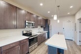 This 2-bedroom, 1-bathroom residence in South Burlington, Vermont offers a thoughtfully designed single-floor layout with modern finishes and a clean, contemporary aesthetic throughout. Light-toned hardwood-style flooring flows consistently across the entire unit, lending a cohesive and airy feel.

The open-concept kitchen, dining, and living area serves as the heart of the home. The kitchen is well-appointed with rich dark-brown cabinetry, stainless steel appliances including a range, microwave, and dishwasher, white quartz-style countertops, and a central island with pendant lighting above — ideal for both meal prep and casual dining.

The living area extends naturally from the kitchen, with large windows that invite abundant natural light and offer views of the surrounding landscape.

Both bedrooms are comfortably sized with continued hardwood-style flooring, white walls, and generous closet space. One bedroom features a large window with scenic outdoor views. The shared bathroom includes a wide vanity with dark cabinetry matching the kitchen, a large mirror, and a tall linen storage cabinet. Additional conveniences include in-unit laundry and multiple closets providing ample storage throughout. The overall ambiance is modern, clean, and functional.