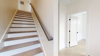 This contemporary 3-floor home is designed with a clean, modern aesthetic and a neutral palette that creates a bright, airy atmosphere throughout. The interior features a mix of light hardwood flooring and polished concrete-style tile, contributing to a cohesive and refined look across all levels. A central staircase with warm wood treads, white risers, and a wood handrail with matte black hardware serves as both a functional and visual anchor connecting all three floors.

The kitchen is outfitted with white shaker-style cabinetry, stainless steel appliances including a range, microwave, dishwasher, and refrigerator, along with recessed lighting and direct access to the adjoining living area. Multiple bedrooms feature light hardwood floors, generous closet space with paneled doors and black hardware, ceiling fans, and windows offering views of surrounding greenery.

Bathrooms range in style, with one featuring elegant marble-look tile flooring, a glass-enclosed walk-in shower, and a white vanity, while others include tub-shower combinations finished in clean white surrounds. Throughout the home, abundant windows fitted with horizontal blinds invite natural light into every room, enhancing the open and welcoming character of this well-appointed multi-level residence.