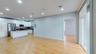 This 2-bedroom, 2-bathroom residence is arranged on a single floor, offering a clean and functional layout. The open-concept living and kitchen area serves as the heart of the unit, where light wood-style flooring flows continuously throughout, lending warmth and visual continuity to the space. Soft blue-gray walls complement the bright, airy atmosphere created by recessed lighting embedded in the white ceiling.

The kitchen is positioned along one wall and features white cabinetry, including glass-front upper cabinets, paired with dark countertops for a modern contrast. Stainless steel appliances, including a microwave and range, are integrated into the design. An electrical panel is conveniently housed within the main living area.

A doorway visible from the main space leads to an adjacent room that benefits from natural light through a window, suggesting a well-connected floor plan. The combination of neutral tones, consistent flooring, and recessed lighting throughout creates a cohesive, contemporary ambiance that is both practical and inviting.