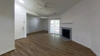 This single-story apartment offers 930 square feet of functional living space across 2 bedrooms, 1 bathroom, and a combined dining room, kitchen, and living area connected by two hallways. The living room is a standout space, featuring rich hardwood-style flooring, a ceiling fan, a tile-surround fireplace with a classic white mantel, and a sliding glass door that opens to a balcony, allowing natural light to fill the room. Adjacent to the living area, the kitchen is designed for efficiency, equipped with stainless steel appliances including a refrigerator, electric range, and over-the-range microwave. White cabinetry and gray countertops extend to a peninsula with a built-in sink, creating a seamless transition between cooking and dining areas. White tile flooring completes the kitchen. The primary bedroom measures 220 square feet and features plush carpet, a large window for natural light, and direct access to the bathroom. The second bedroom is also carpeted with a window and ample wall space. The shared bathroom includes a full tub-shower combination with classic white tile surround and chrome fixtures. Hallways connect the rooms efficiently, and the entry area includes a closet alongside the front door.