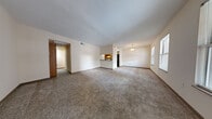 This single-floor unit offers three bedrooms and one bathroom within a efficiently organized floor plan connected by two hallways. The open-concept living room is generously proportioned for the overall footprint, featuring neutral-toned carpet, textured ceilings, and a pass-through opening that connects directly to the kitchen, enhancing the sense of openness between the two spaces.

The kitchen is equipped with wood-toned cabinetry, a electric range, dishwasher, and a refrigerator. Tile flooring runs throughout the kitchen, and a louvered utility closet provides additional storage. A pendant light fixture adds a subtle decorative accent above the pass-through counter.

The three bedrooms are carpeted and finished with neutral walls and dark baseboards. The primary bedroom is the largest of the three, featuring multiple windows that bring in natural light and a closet with sliding doors. The secondary bedrooms are more compact, each with carpet and standard electrical fixtures.

The single bathroom includes a full tub-shower combination with tiled surround, a toilet, and tile flooring in a clean, neutral palette. Two hallways connect the living areas to the bedrooms and bathroom, contributing to a straightforward and functional layout throughout the unit.