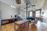 Located at 1082 RT-79 in Fall River, MA, this single-floor space showcases an impressive loft-inspired design that blends industrial character with modern comfort. The generously sized living room is the centerpiece of the space, boasting soaring ceilings with exposed ductwork, original structural columns, and warm hardwood floors throughout. A striking exposed brick wall frames two large windows that flood the room with natural light, while curated wall art, a tufted teal sofa, and a stainless steel kitchen area with ample counter space contribute to the room's refined yet relaxed atmosphere. A separate seating nook with a wall-mounted TV offers a quieter retreat within the open layout. The game room is a standout feature, centered around a full-size pool table beneath a large drum pendant light. Leather bar stools, a lounge sofa, a wall-mounted TV, and exposed ceiling ductwork reinforce the industrial aesthetic, creating an inviting entertainment environment. The bathroom is thoughtfully designed with ADA-compliant features, including grab bars, a floating vanity with granite countertop, large-format tile flooring, and modern fixtures, ensuring both accessibility and style. Together, these spaces deliver a cohesive, versatile environment ideal for entertaining, relaxing, or gathering.